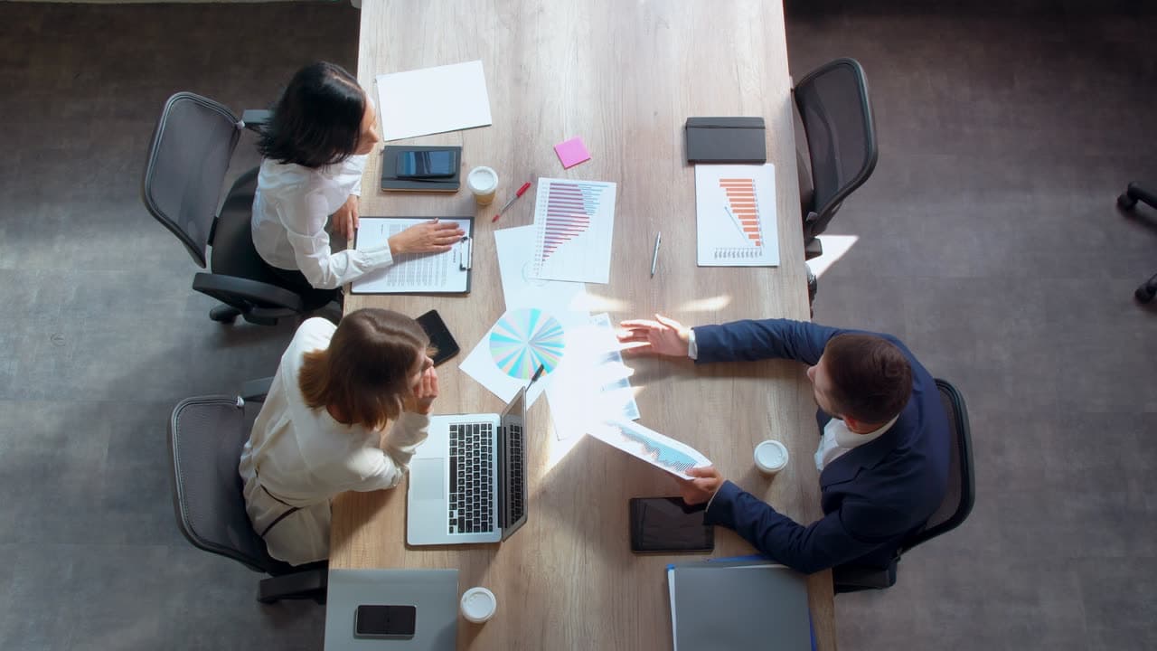 A small business team meeting around a table covered in reports