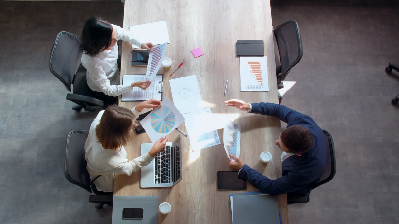 A small business team meeting around a table with laptops and reports